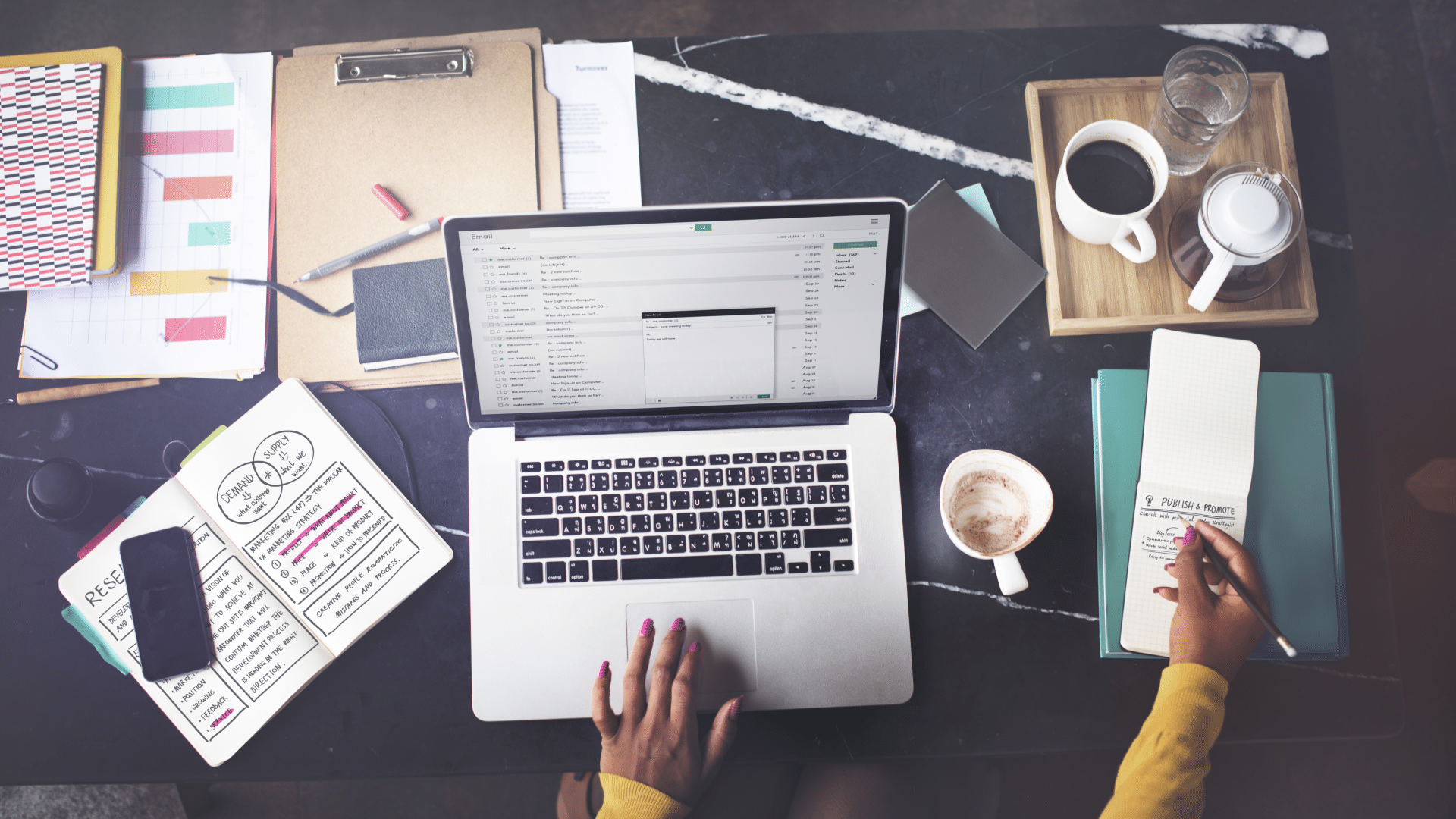 a person writes an email while surrounded by paperwork on a desk